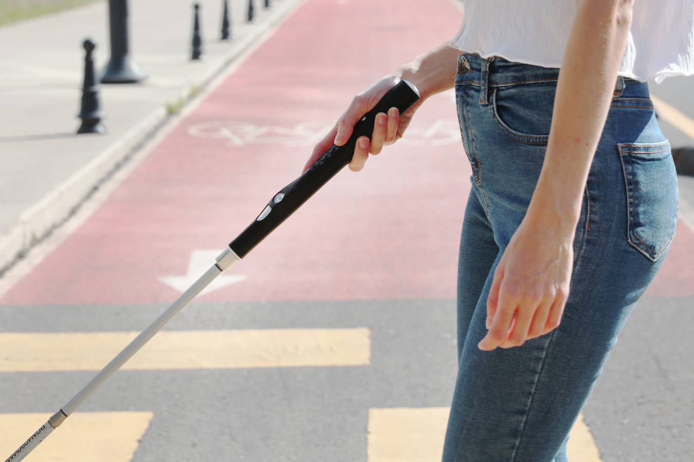 Side view of a woman navigating a crosswalk with the aid of the Smart Cane 2, a tech-enabled white stick by WeWALK
