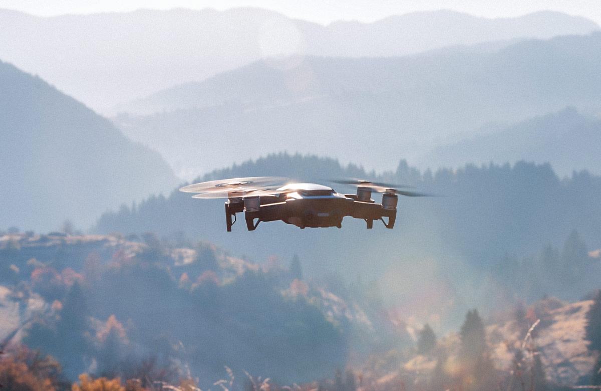 Small modern drone hovering taking picture of a sunrise in a mountain range