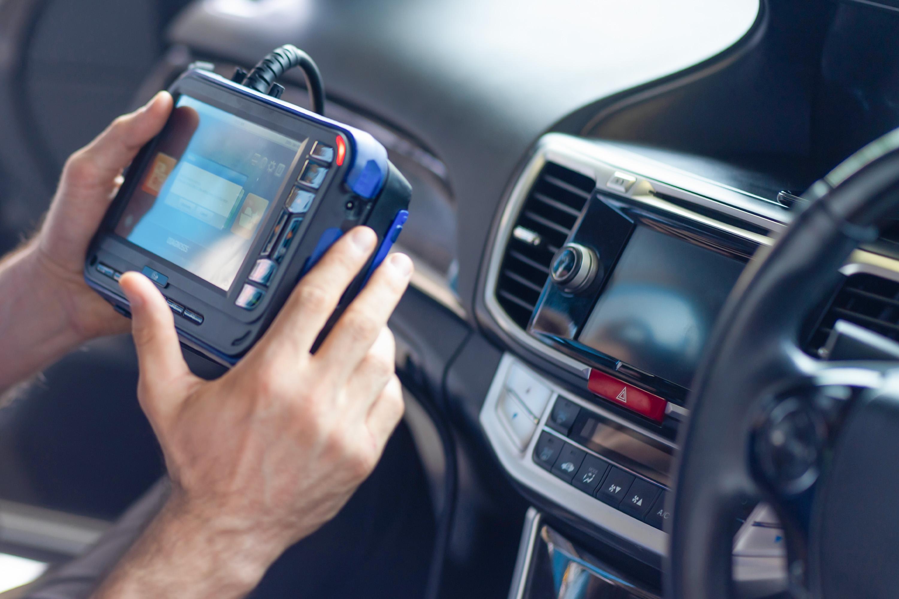 Photograph of interior of car with a pair of hands holding a diagnostic device for vehicles