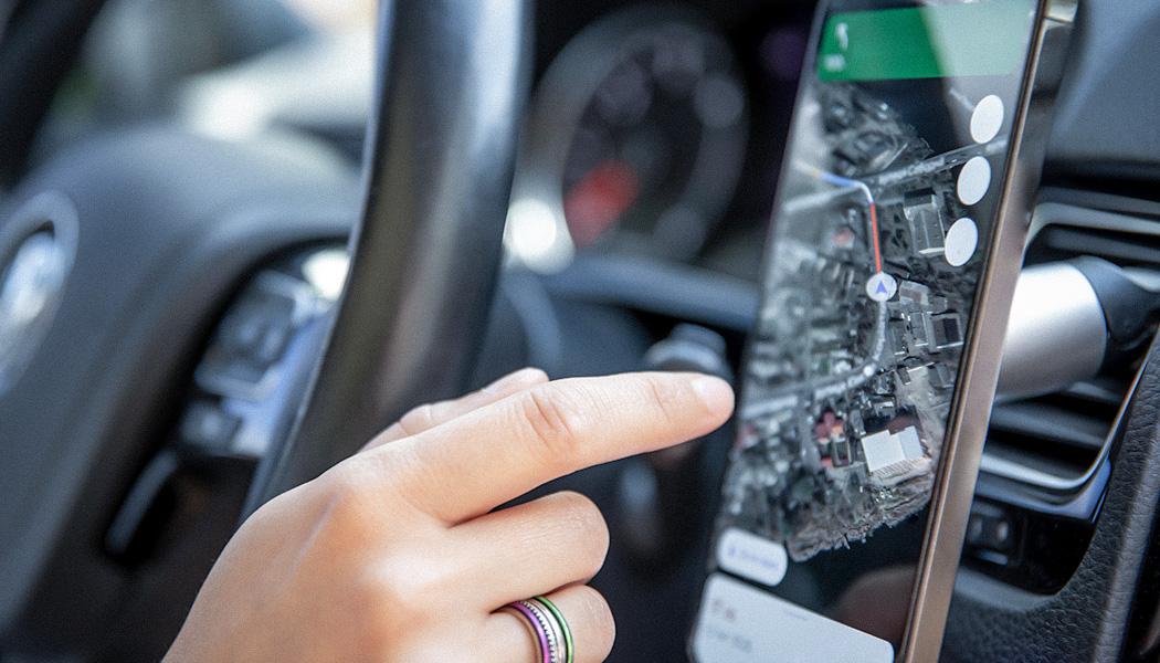 Driver’s hand holding a phone with interface navigator on a screen.