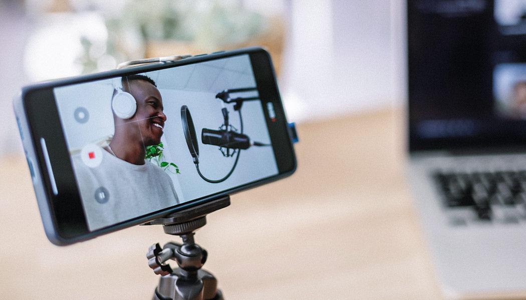 Photo of smartphone screen recording man speaking into studio microphone