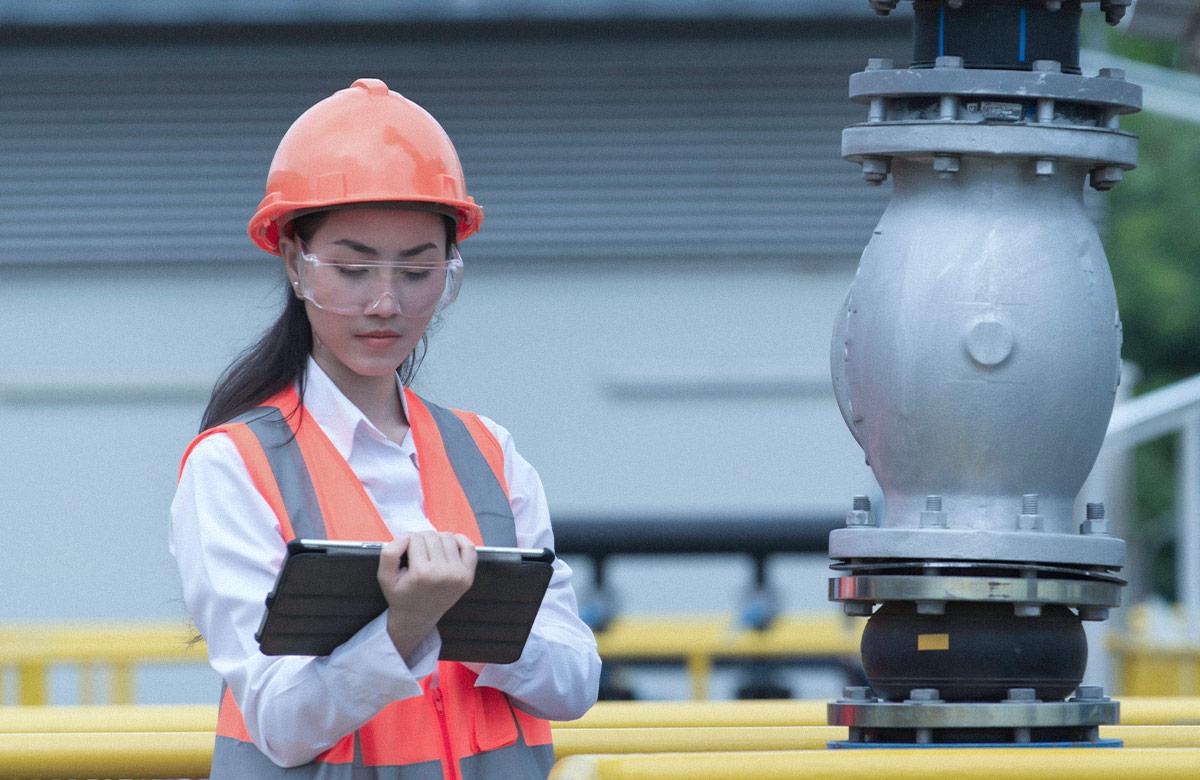 Photo of a woman in an industrial environment wearing goggles and holding a digital tablet