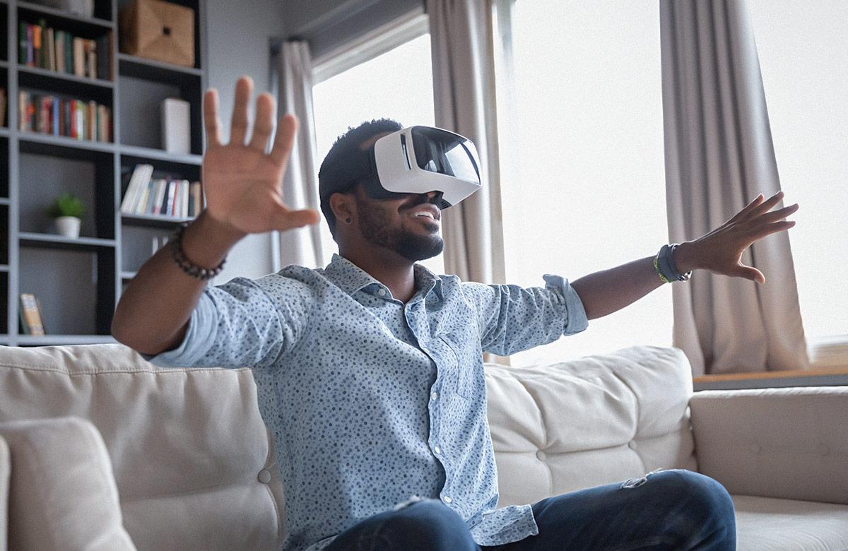 Man sitting on couch wearing virtual reality headset and gesturing with his arms