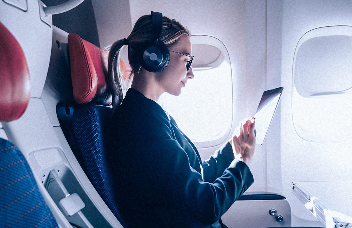 Woman sitting in plane with over-ear headphones holding tablet device
