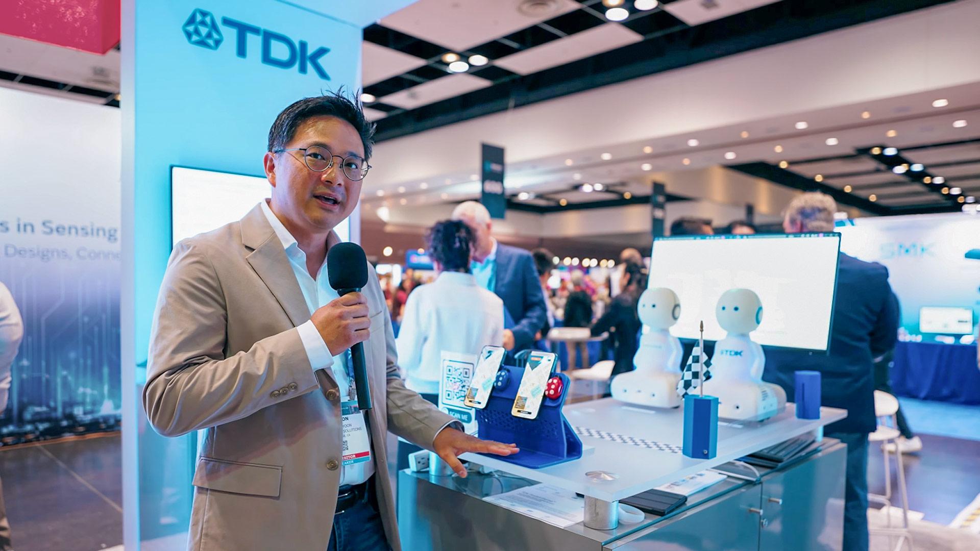 Photograph of a man holding a microphone in front of a product demo display at a trade show