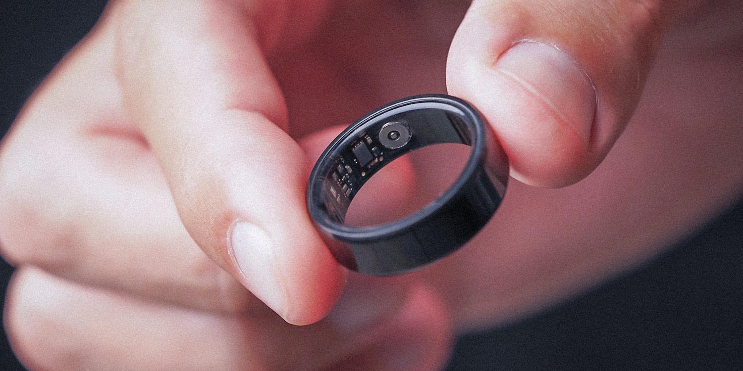 Detailed photograph of a hand holding a smart ring, a health device worn around the user’s finger