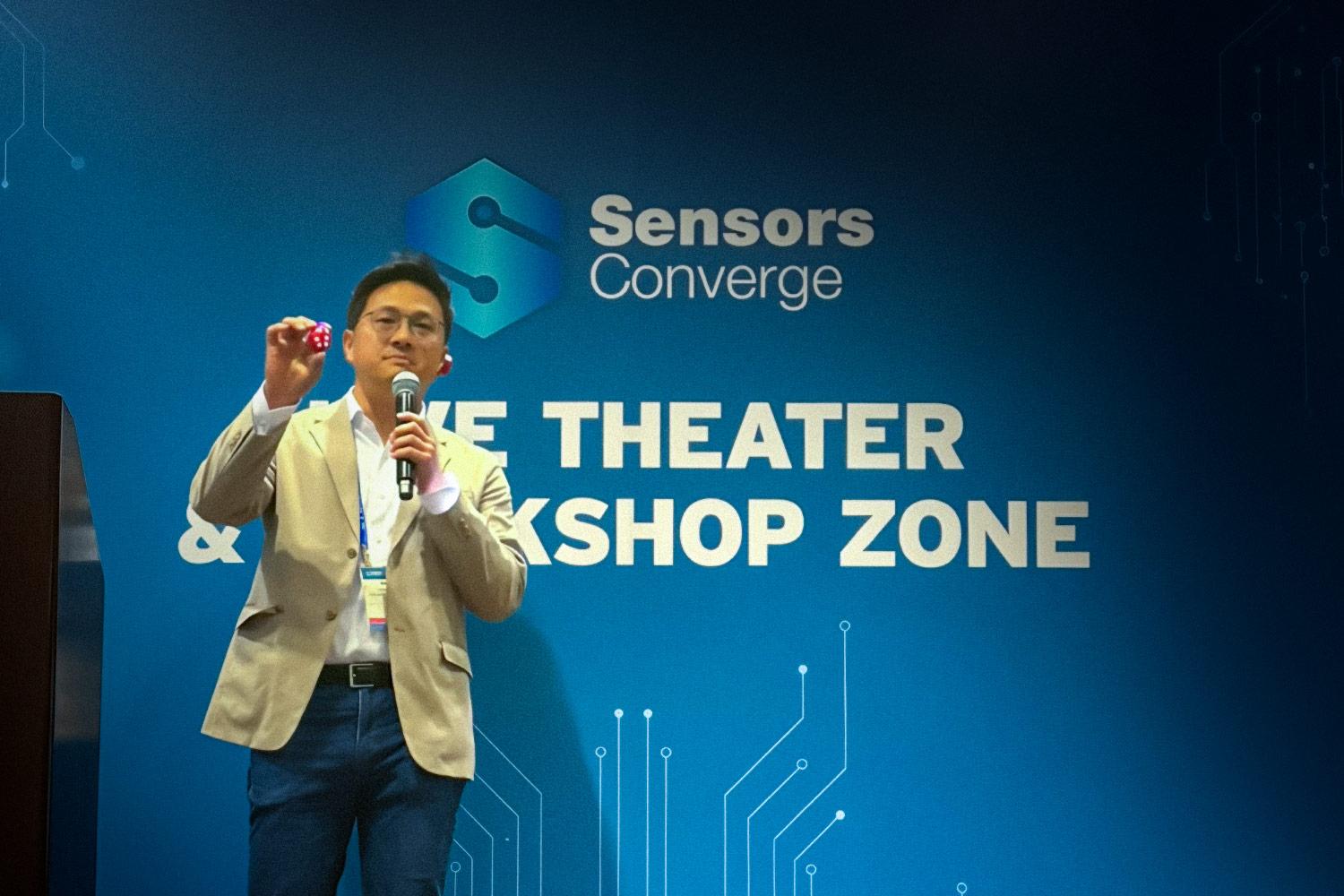 Man with microphone on stage holding up an electronic device