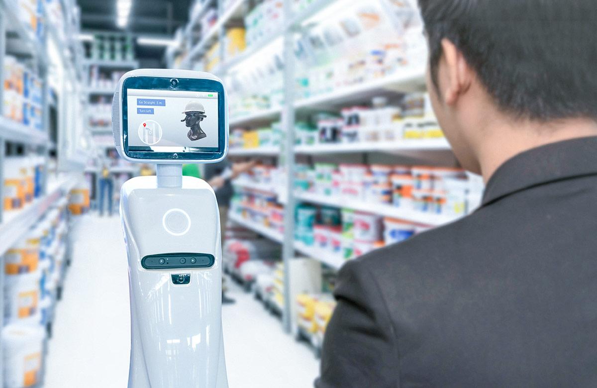 A white, cylindrical service robot with a screen, providing navigation instructions in a store aisle, while a person is looking towards the robot.