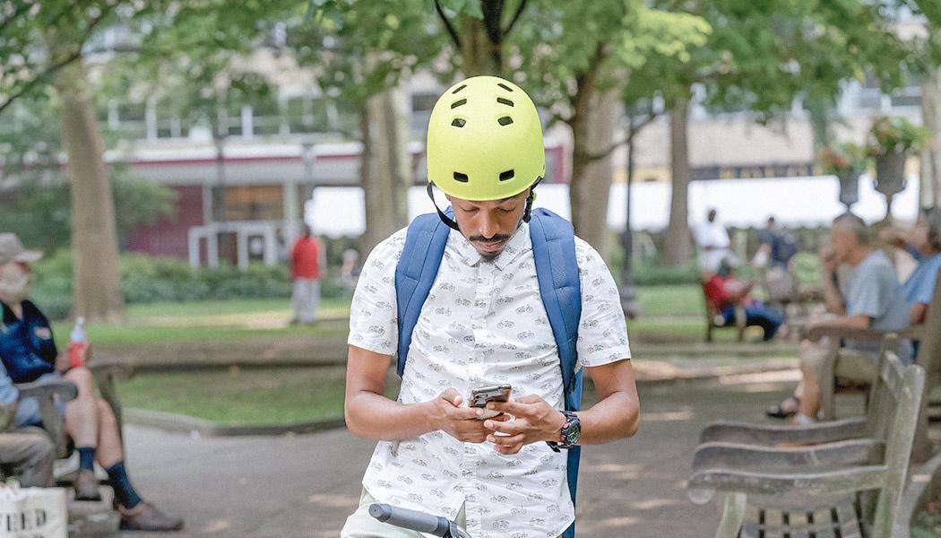 Man wearing yellow bicycle helmet sitting on bicycle uses his smart phone in park