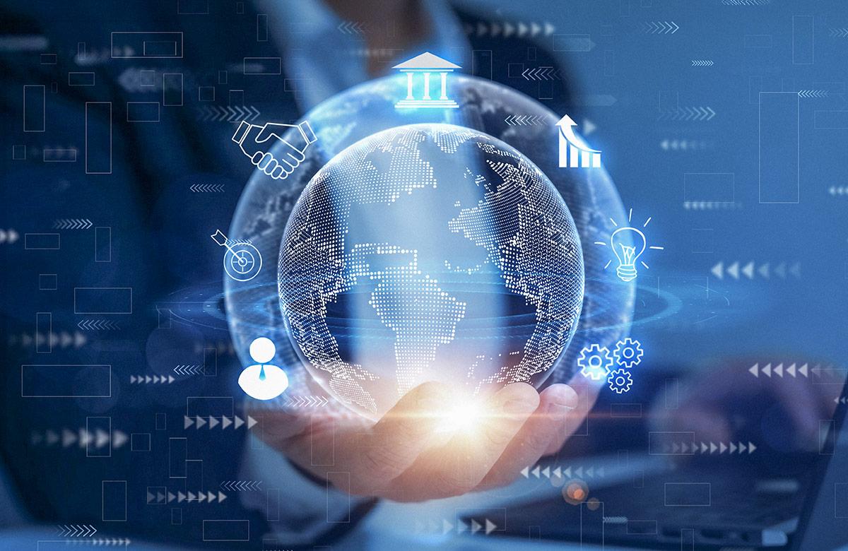 A businessman’s hand holding a glowing digital globe surrounded by icons of business and finance, with a laptop in the background, set against a blue, tech-focused backdrop.