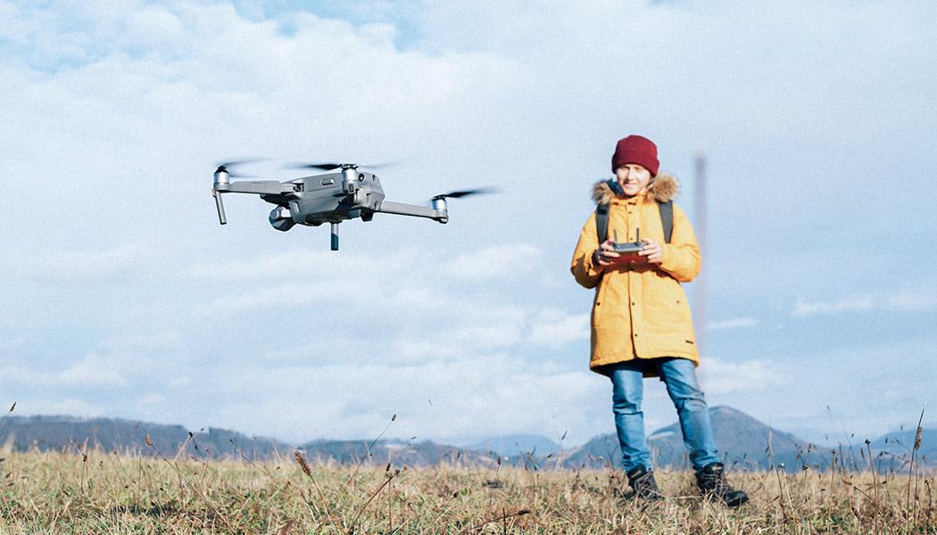 Young boy dressed yellow jacket on in open field piloting a modern digital drone using remote controller