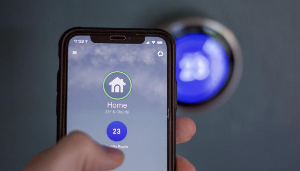 Close-up of hand using smartphone to change the temperature of smart home thermostat